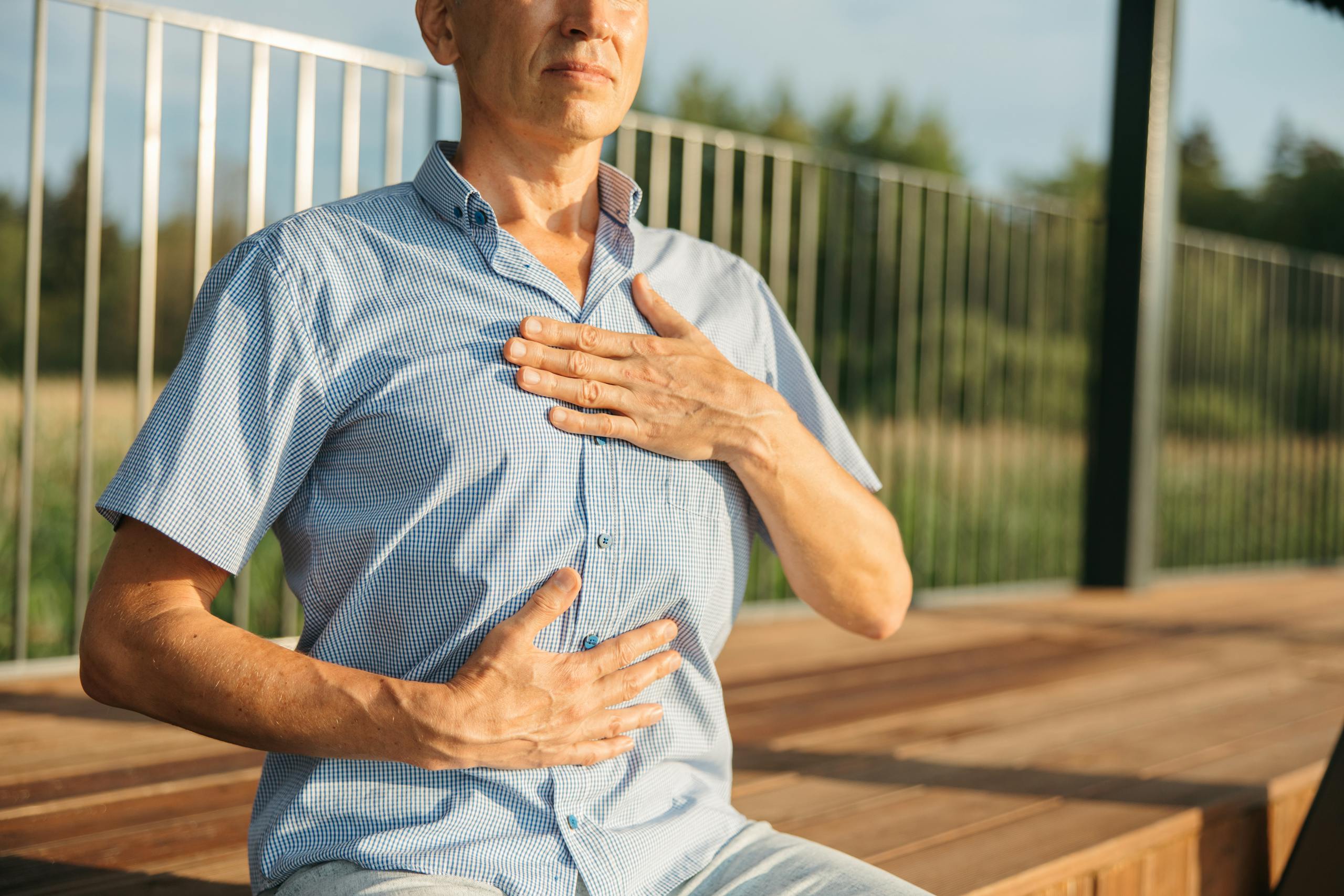 Behavioral medicine approach: a man practicing relaxation with hands on chest and abdomen outdoors.